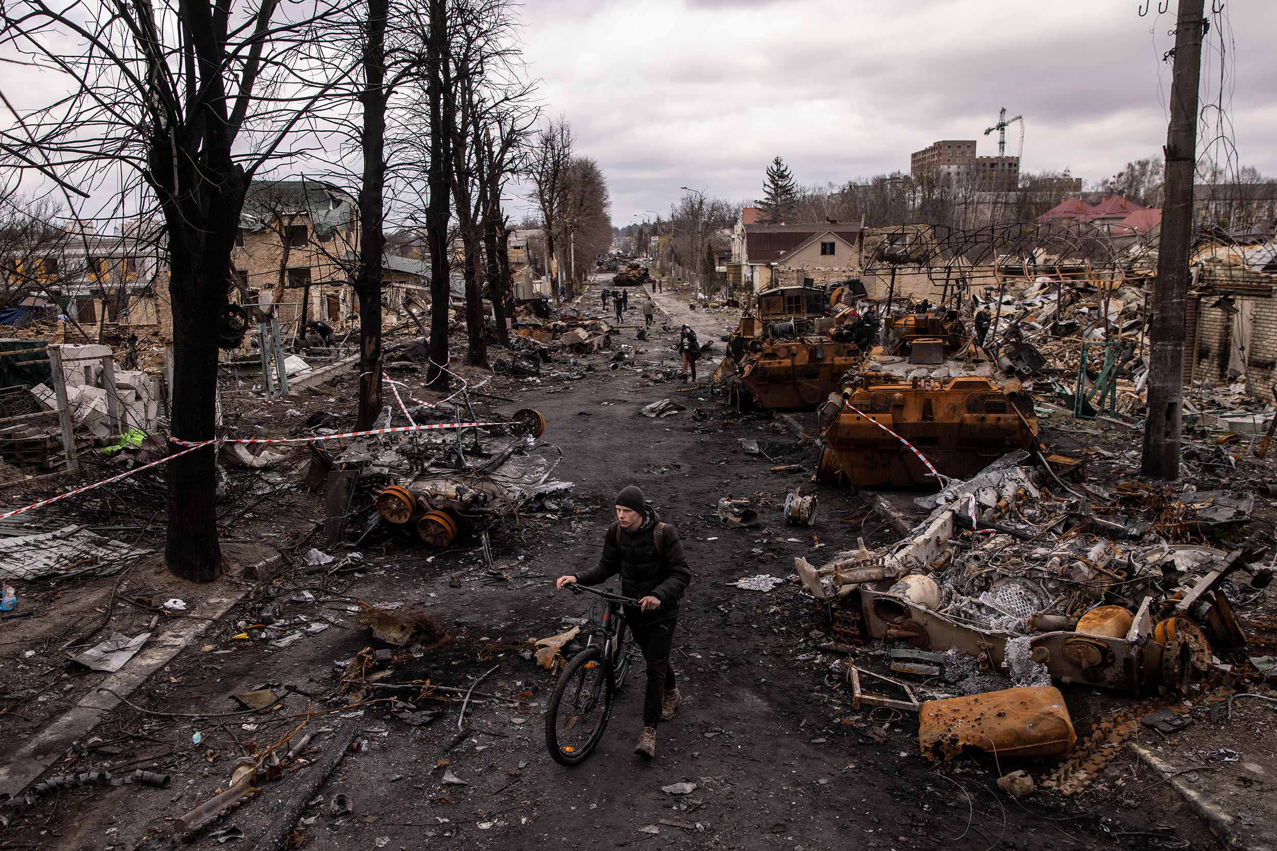 A man pushes his bike through debris and destroyed Russian military vehicles on a street on April 06, 2022 in Bucha, Ukraine. The Ukrainian government has accused Russian forces of committing a "deliberate massacre" as they occupied and eventually retreated from Bucha, 25km northwest of Kyiv. Hundreds of bodies have been found in the days since Ukrainian forces regained control of the town. © Chris McGrath/Getty Images