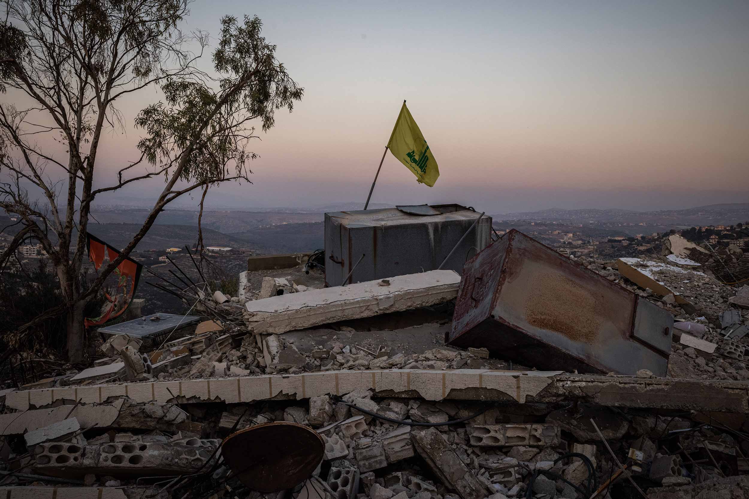 A Hezbollah flag stands on rubble left by an Israeli airstrike on December 3, 2024 near Kherbet Selem, Lebanon. Israel and Hezbollah had agreed to a truce in late November, aiming to end 13 months of hostilities. It has proven fragile in the days since, with each side accusing the other of violations. © Ed Ram/Getty Images