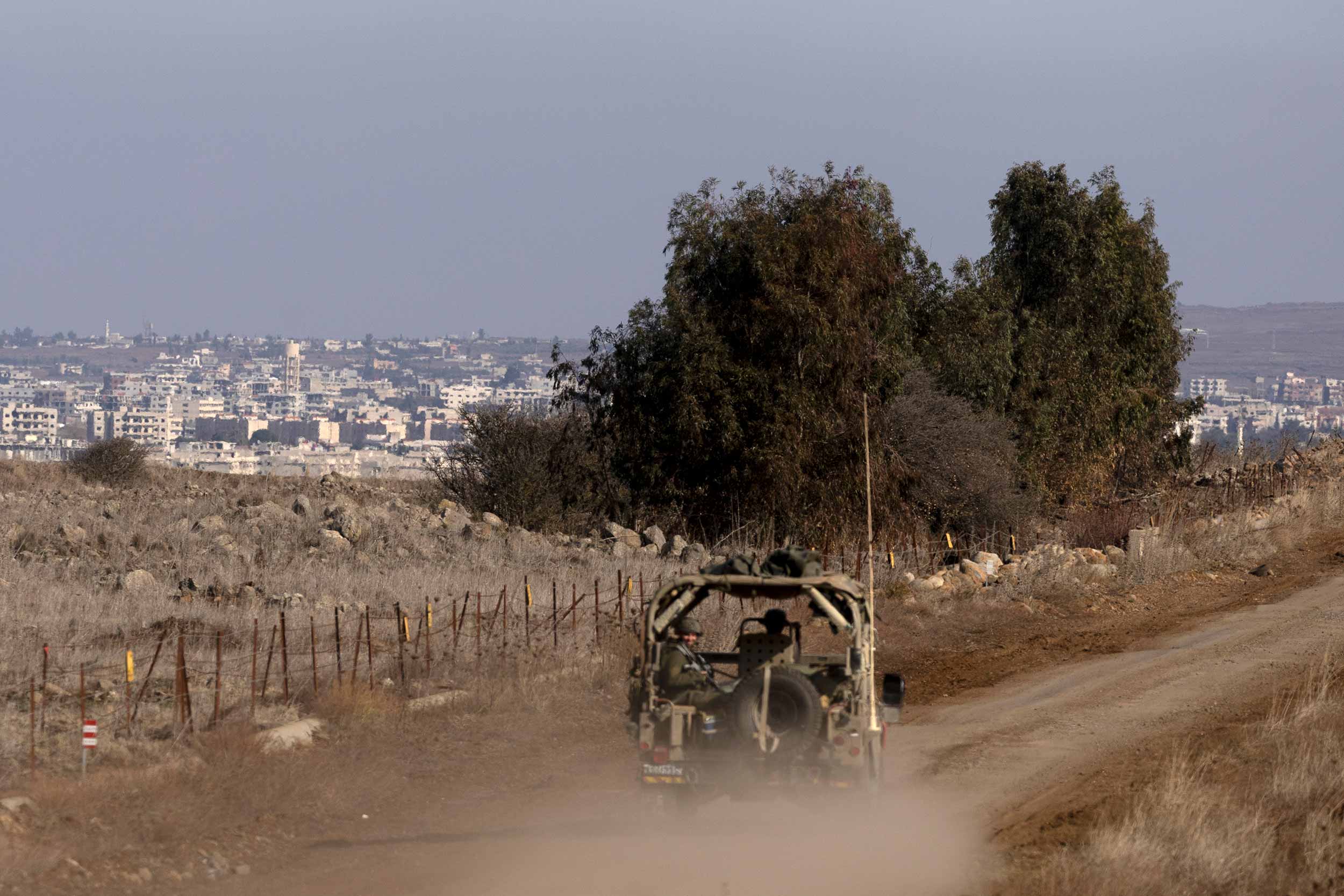 An Israeli army vehicle is driven along the border with Syria with the village of El Hmidaiah in the background on December 9, 2024 in Golan Heights. Israeli Prime Minister Benjamin Netanyahu has ordered the Israel Defense Forces (IDF) to temporarily take control of a buffer zone that separates the Israeli-occupied Golan Heights from Syrian territory. © Amir Levy/Getty Images