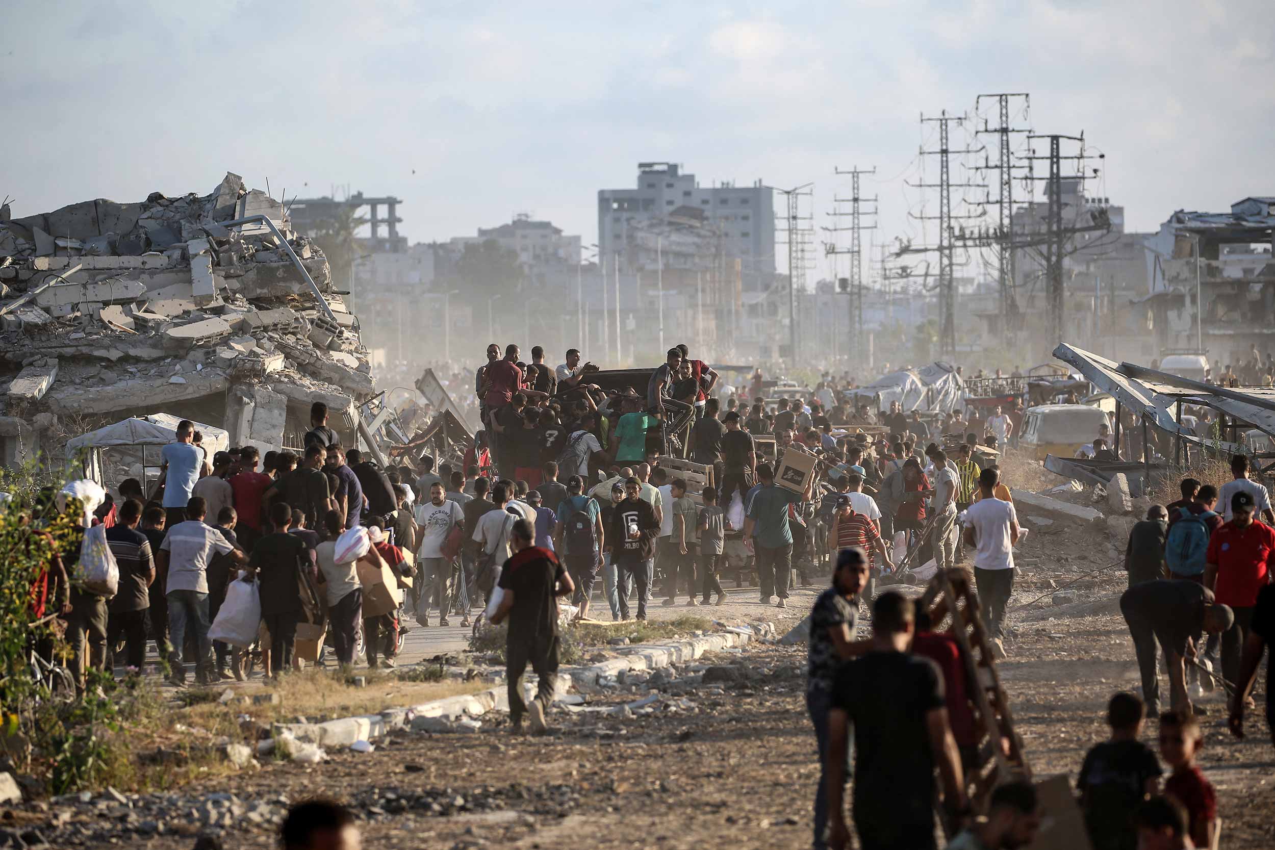 People carrying aid parcels, walk along the Salah al-Din road near the Nusseirat refugee camp in the central Gaza Strip, used by food-seeking Palestinians to reach an aid distribution point set up by the privately-run Gaza Humanitarian Foundation (GHF), on June 25, 2025. © Eyad BABA / AFP