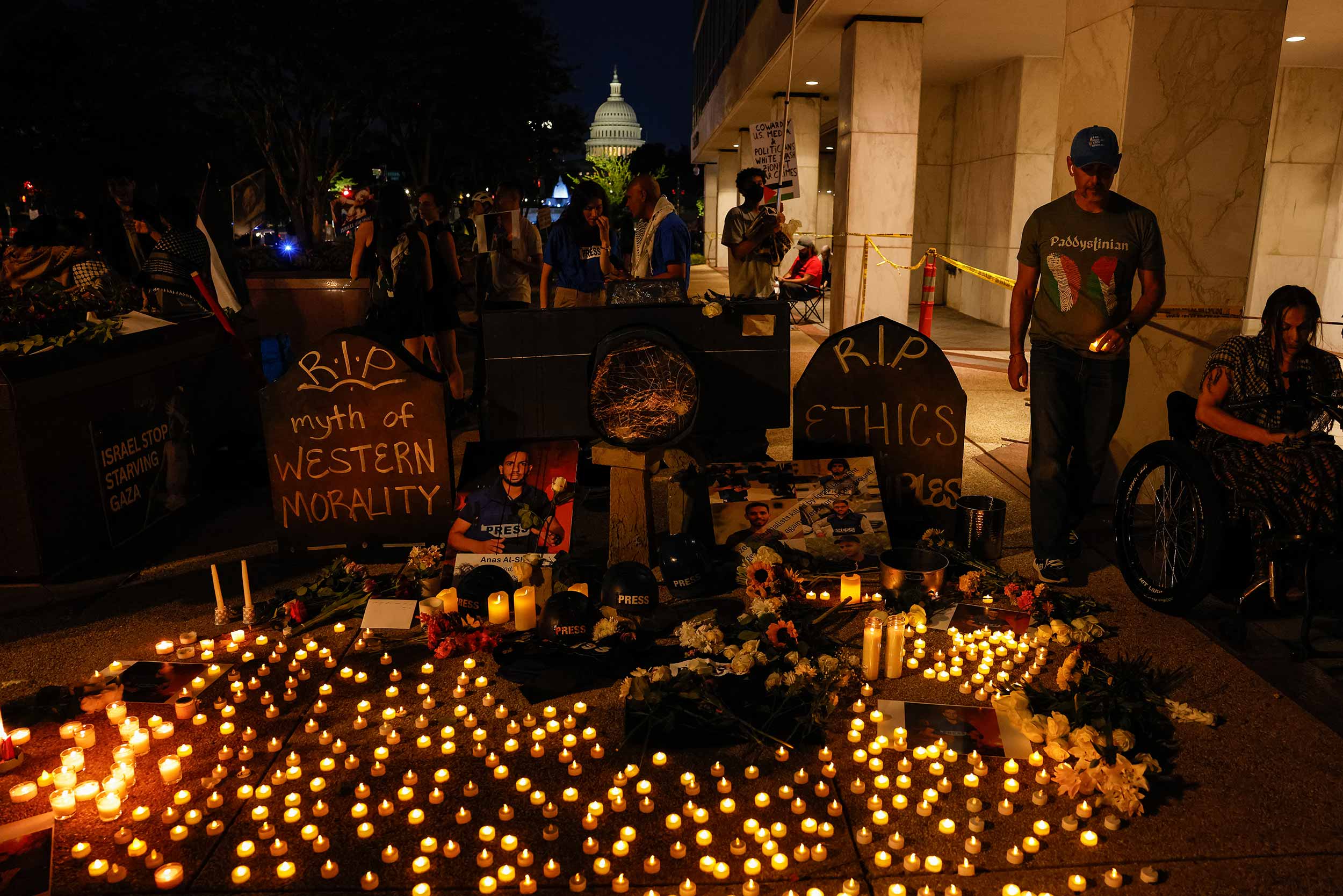 People hold photos, lay flowers and light candles during a vigil outside the Fox News and NBC News headquarters in Washington, D.C., August 11, 2025, honouring journalists killed in Gaza, including Anas al-Sharif and his colleagues. © Mehmet Eser/Middle East Images/AFP via Getty Images