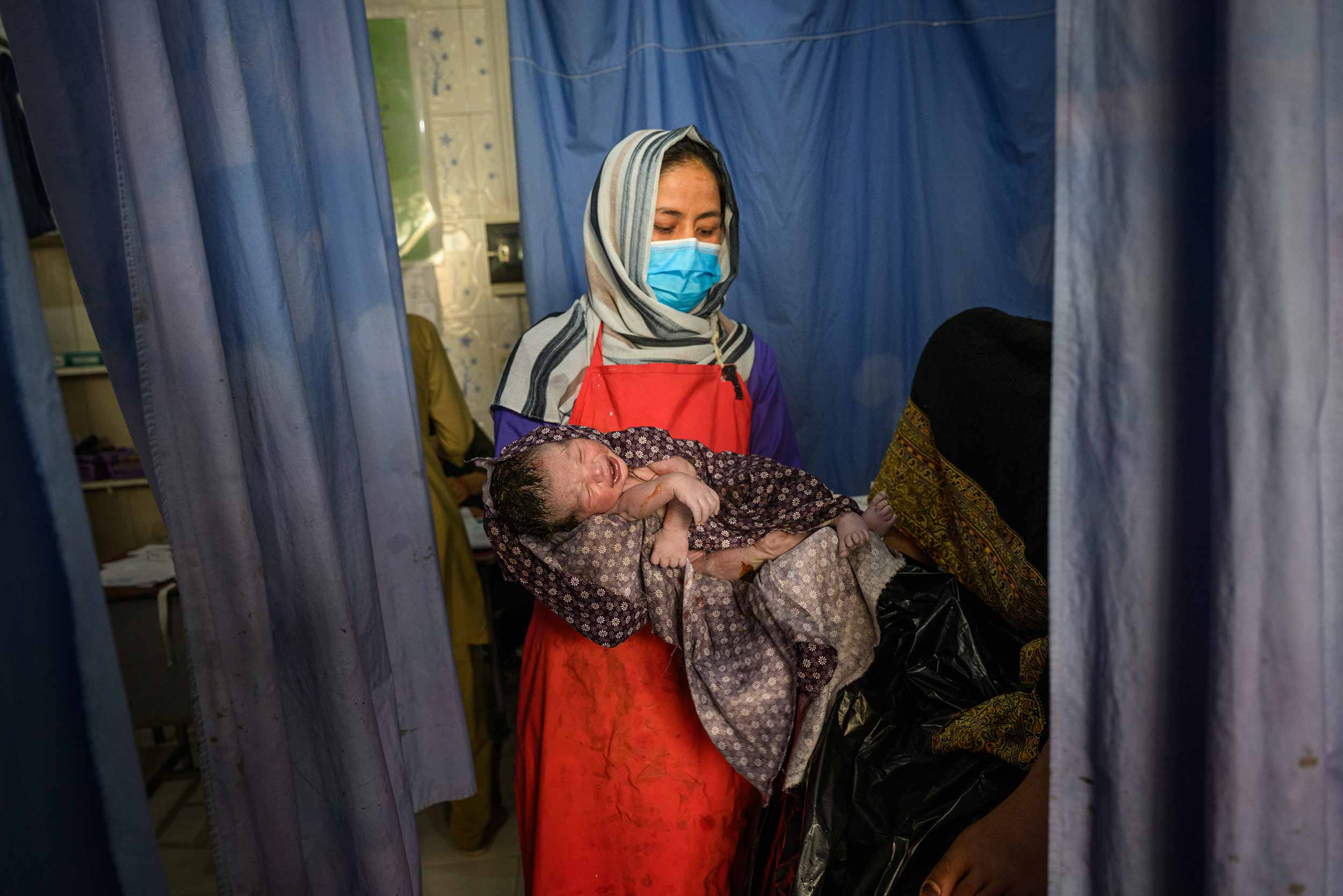 Midwife Samonah, 33, holds a newborn after a delivery at the provincial hospital's maternity unit on August 27, 2025, in Ghazni, Afghanistan. Of the 422 health facilities that have been suspended or closed in Afghanistan since the termination of USAID funding thirty of the closures have taken place in the Ghazni region, affecting more than 226,000 people. © Elise Blanchard/Getty Images