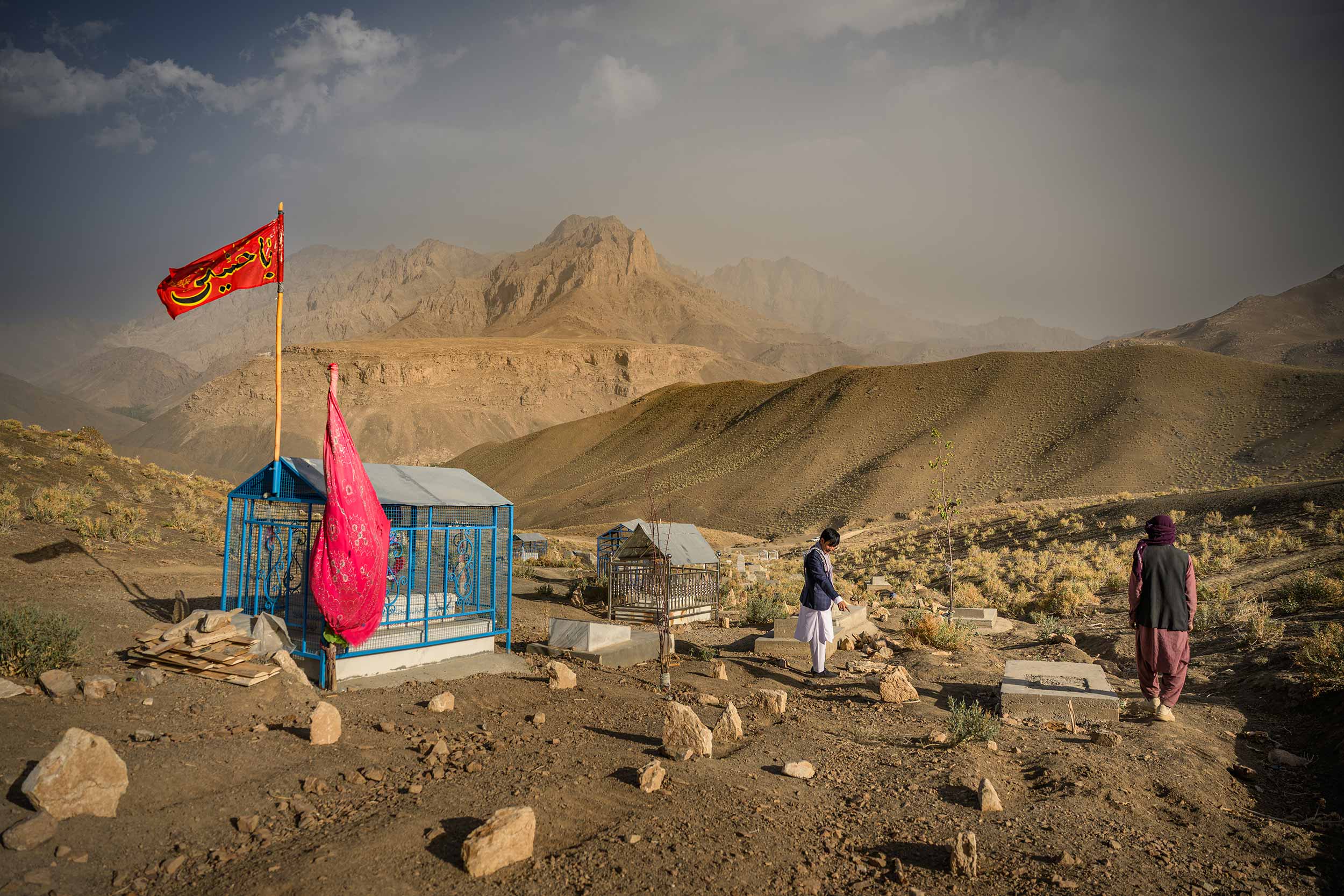 Habibullah Saadat (centre), the guard of the Kamarak clinic, showing the graves of women whose deaths villagers attribute to the closure of the local clinic due to US funding cuts at the end of January, on August 25, 2025, in Jaghori district of Ghazni province, Afghanistan. The closure has left the 9000 inhabitants of the remote village cut off from health services, as other clinics are too far away, with no paved roads, and most people too poor to afford a vehicle to go. © Elise Blanchard/Getty Images
