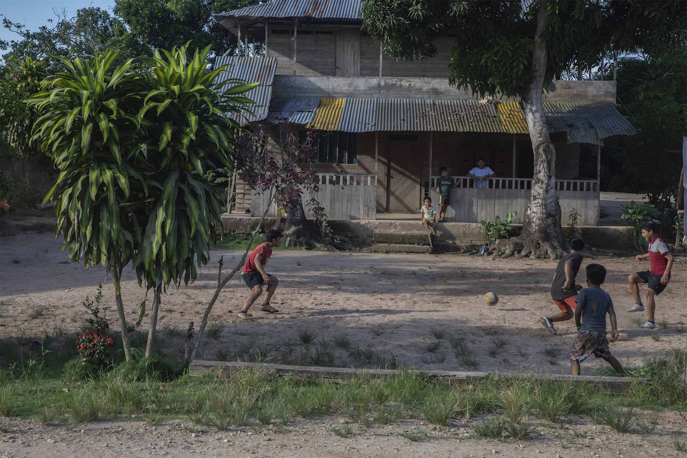 A group of kids play soccer while the adults are gathered in the community center. © Mongabay
