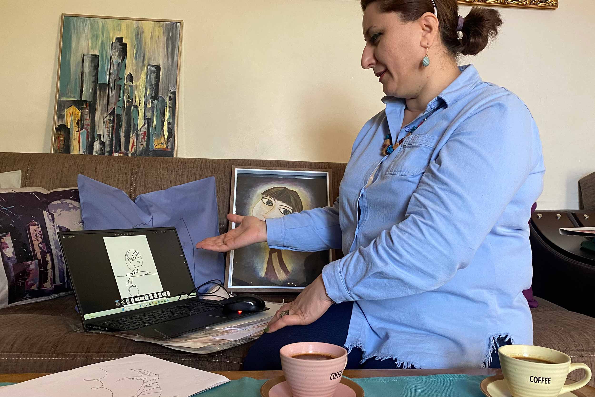 Srbuhi Vanyan, ex presentadora de radio convertida en artista, sentada en su sala de estar en Stepanakert, rodeada de su obra de arte. Debido al bloqueo, su negocio de arte se detuvo. La mujer de 43 años no ha visto a su esposo ni a su hija mayor desde diciembre de 2022, ya que ambos estaban en Ereván cuando se bloqueó el corredor de Lachin. © Siranush Sargsian