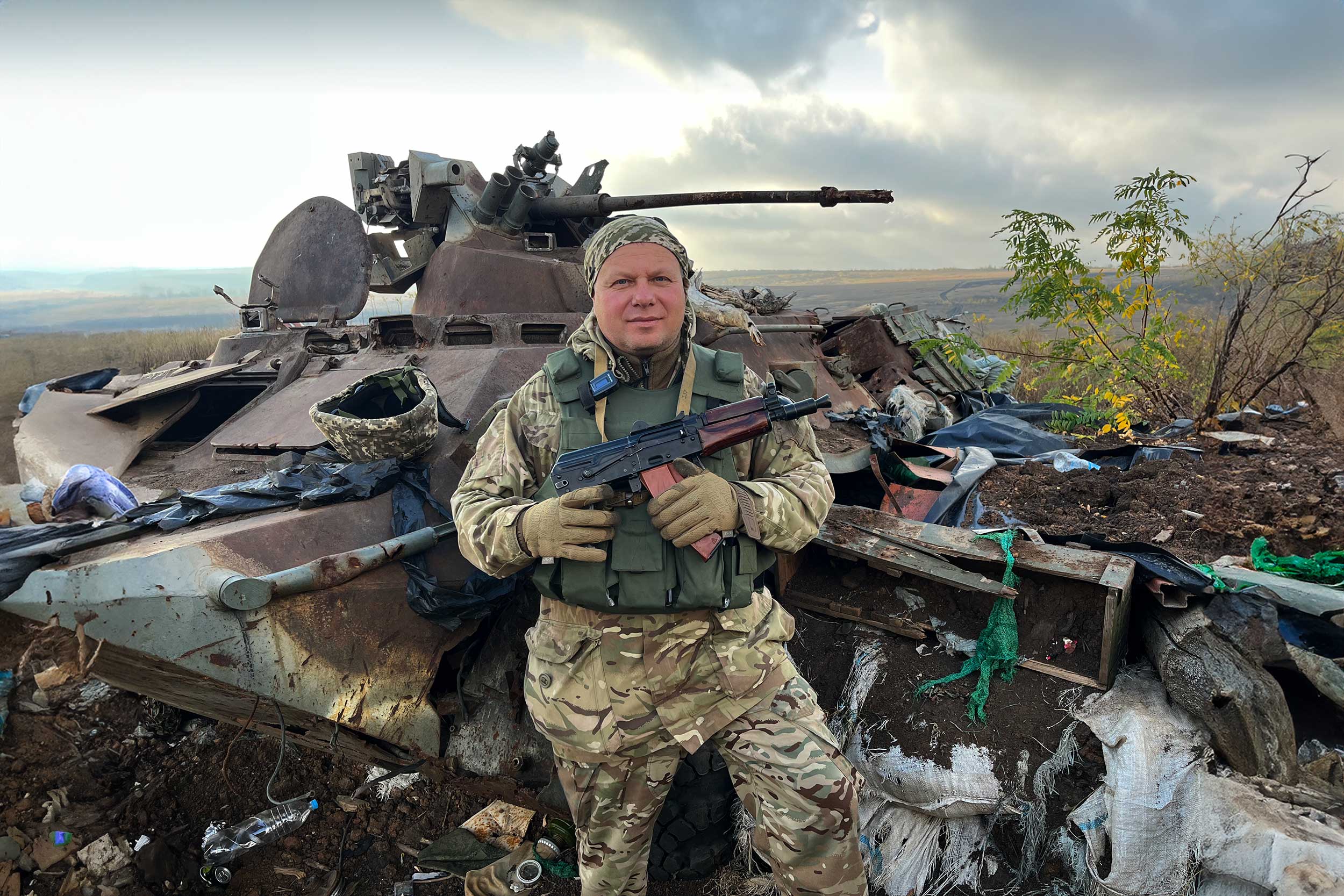 Sergii, an officer of the 65th Mechanised Brigade, in front of a destroyed Russian armoured personnel carrier (APC), on the hilltop Position X, in the Zaporizhzhia region. The APC served as a blindage, or protected dugout for Russian troops, and was the first location Ukraine troops seized in securing the trenches, which commanded the road below, running south. © IWPR
